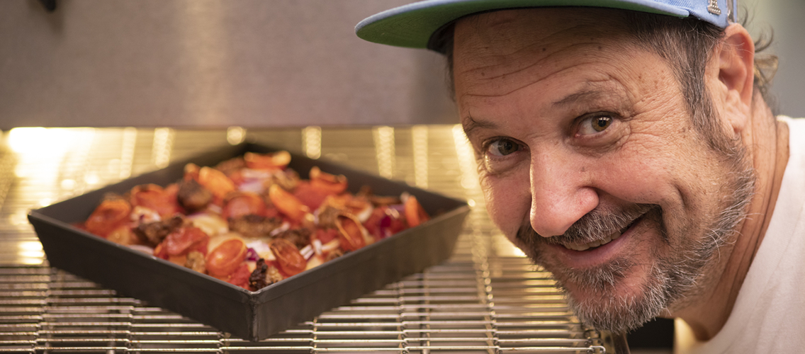 photo of Chef Fred Eric next to an oven with a pizza inside